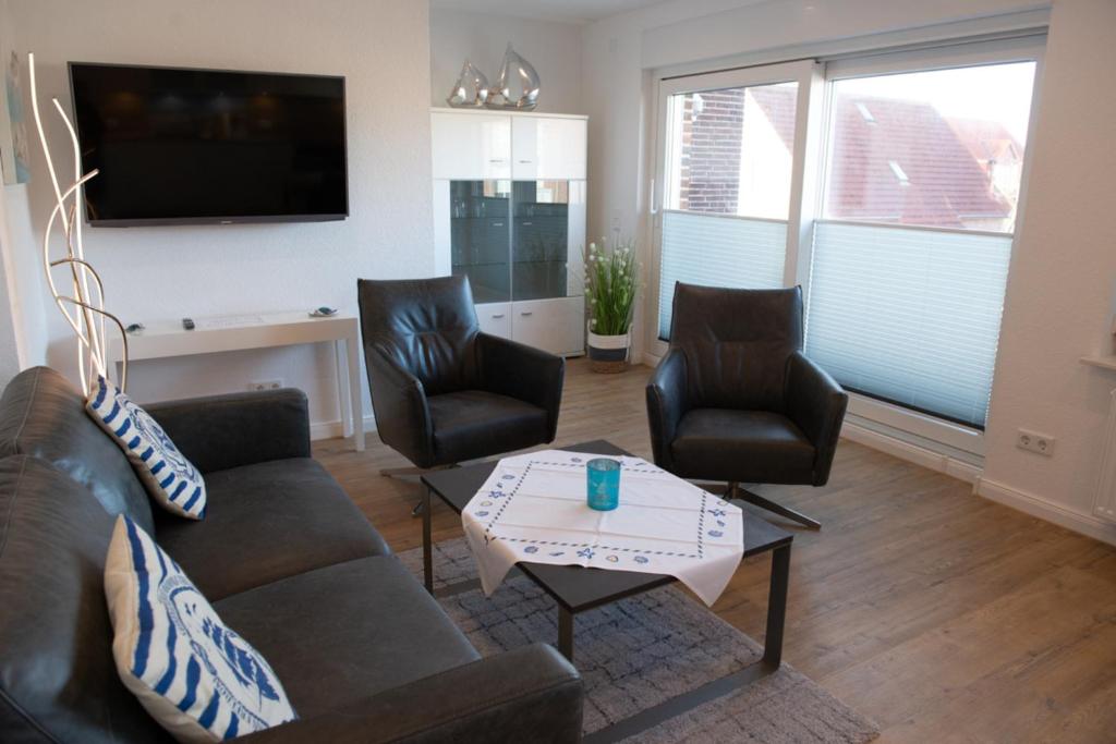 a living room with a couch and two chairs and a tv at Mole links in Norddeich