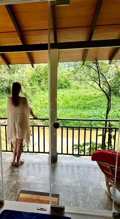 una donna in piedi su un balcone che guarda fuori da una finestra di Rainforest River Bay a Deniyaya