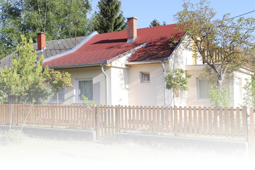 a white house with a fence and a red roof at Balaton Holiday Home in Balatonmáriafürdő