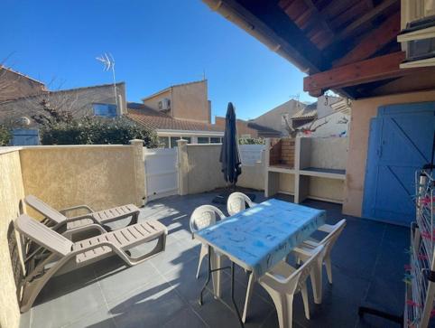 un patio avec une table, des chaises et un parasol dans l'établissement Jolie maison de vacances rénovée et climatisée, 5 couchages, 2 chambres et mezzanine, 100m de la plage, residence LE VILLAGE DE LA MER LRVM39, à Portiragnes