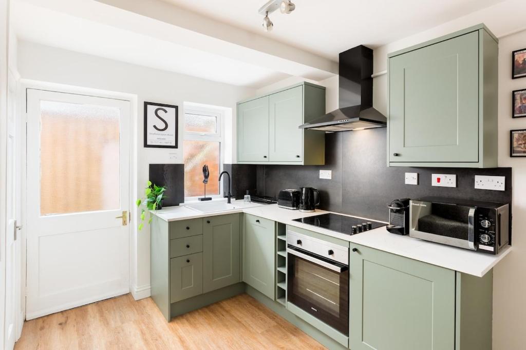 a kitchen with green cabinets and white counter tops at Stylish 2-Bedroom Townhouse in Stratford upon Avon in Stratford-upon-Avon