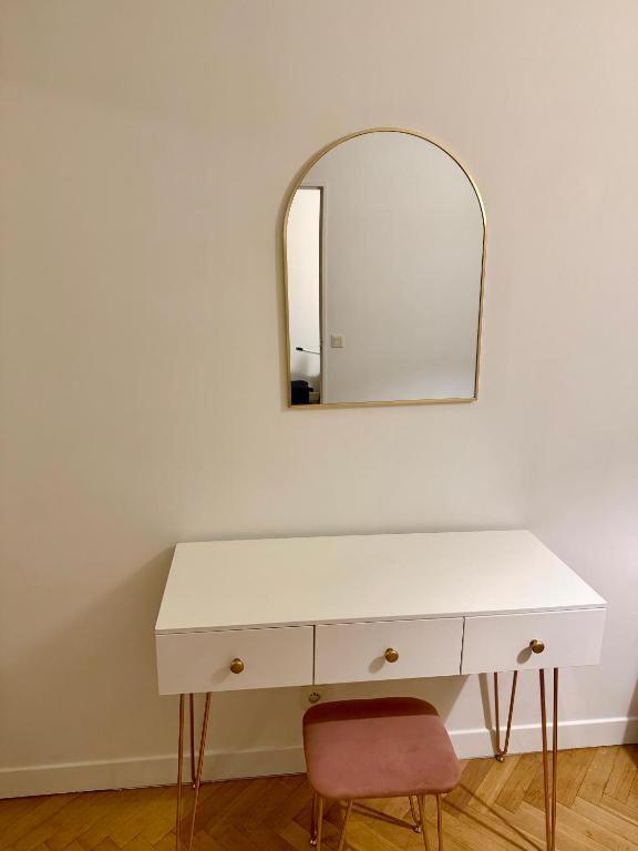 - une commode blanche avec un miroir et une chaise rouge dans l'établissement L'Ilios Cosy House - F2 Lumineux plein centre ville, à Alfortville