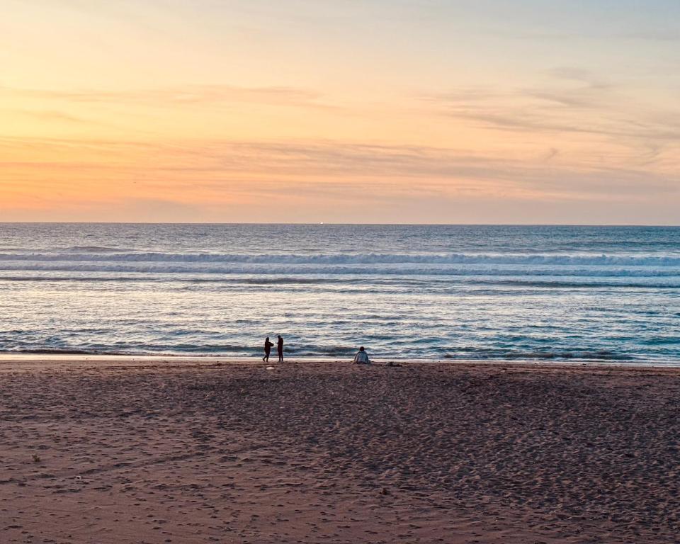 two people standing on a beach with the ocean at Hotel Al Alba Hammam & Restaurant in Asilah