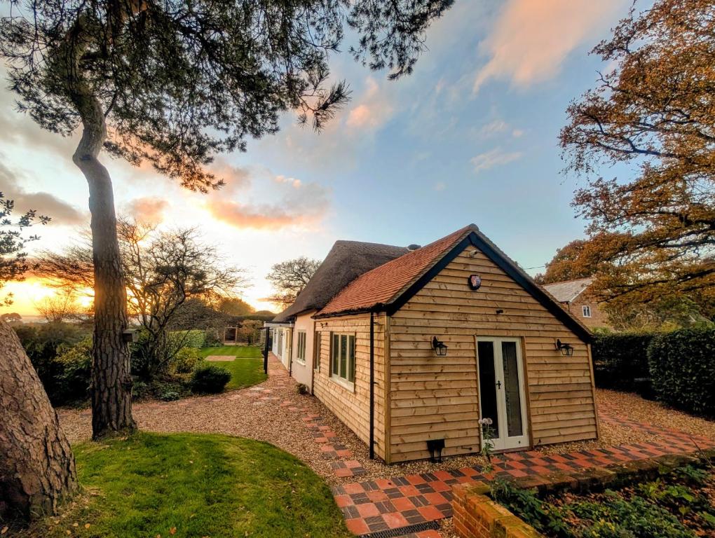 Ein kleines Haus in einem Garten mit dem Sonnenuntergang im Hintergrund in der Unterkunft Stunning New Forest Country House - Abbot's Well for up to 10 guests in Godshill