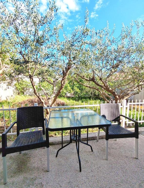 Una mesa de cristal y dos sillas junto a un árbol. en Altura Rooms & Apartments, en Neum