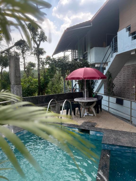 um pátio com uma mesa e um guarda-sol ao lado de uma piscina em Coorg Sana Riverside em Suntikoppa