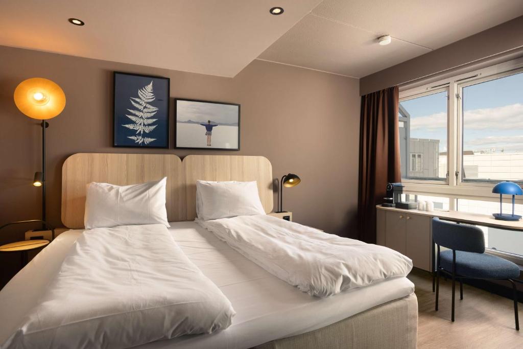 a bedroom with a white bed with a desk and a window at Scandic Victoria in Oslo