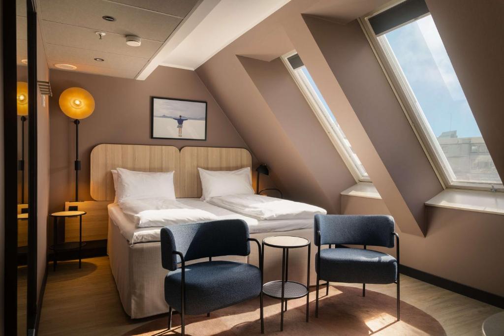 a bedroom with a bed with two chairs and two windows at Scandic Victoria in Oslo