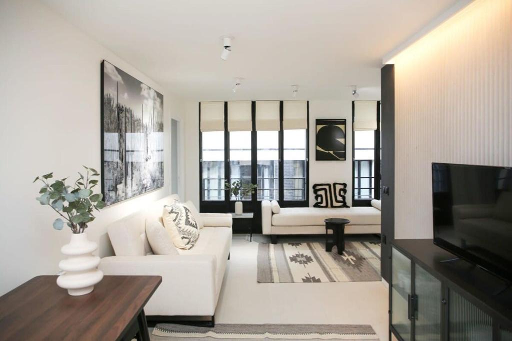 Il comprend un salon doté d'un mobilier blanc et d'une télévision à écran plat. dans l'établissement Espace et Confort en Famille - Marais a Cote - 6P, à Paris