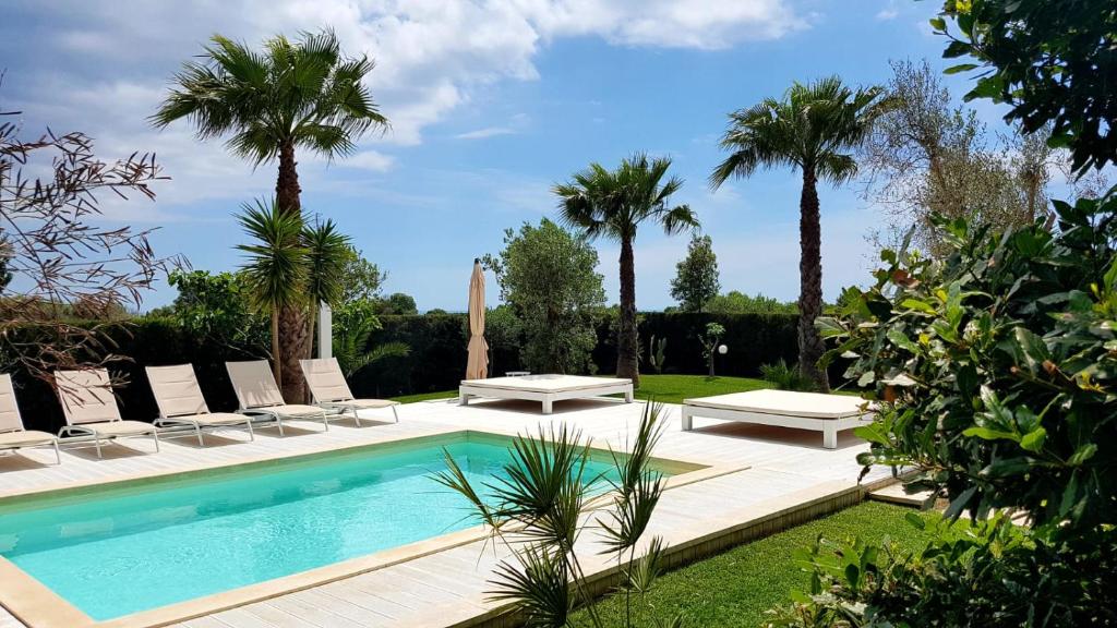 une piscine avec chaises longues et palmiers dans l'établissement Villa Gina by Perle di Puglia, à Torre San Giovanni