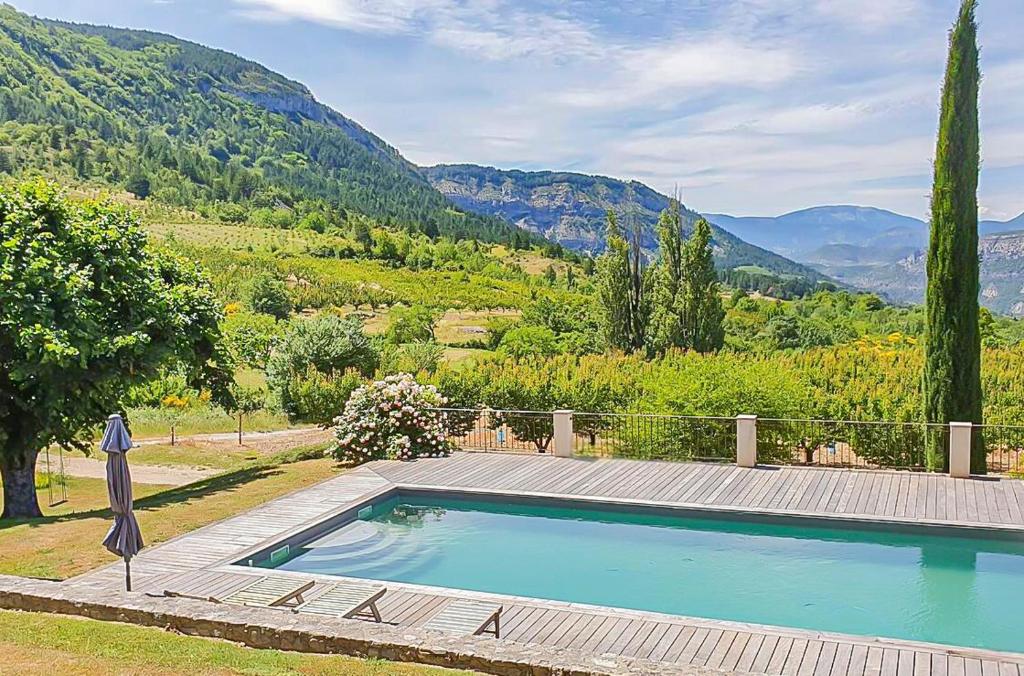 une piscine avec une terrasse en bois et des montagnes en arrière-plan dans l'établissement Maison authentique en Drôme Provençale, à Montréal-les-Sources
