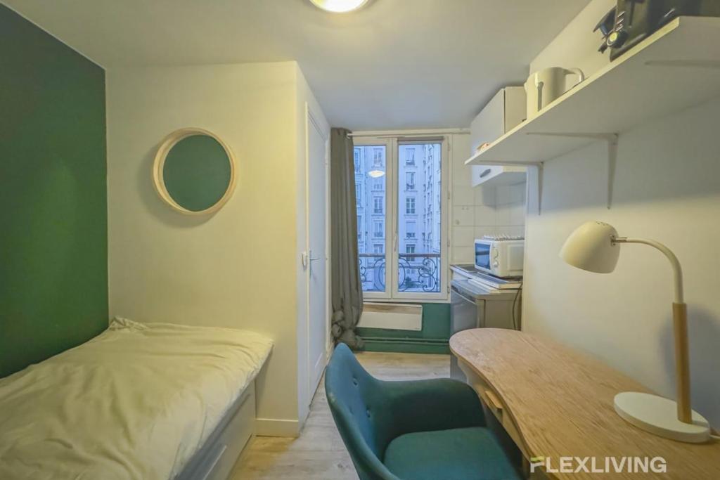 Cette petite chambre comprend un lit, une table et une fenêtre. dans l'établissement Flexliving - Studio - Saint Martin, à Paris