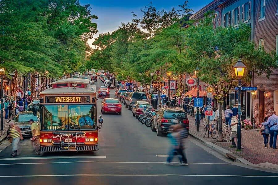 a bus driving down a busy city street with cars at ALX Cape Cod 3-BR Near Old Town & Mount Vernon in Alexandria