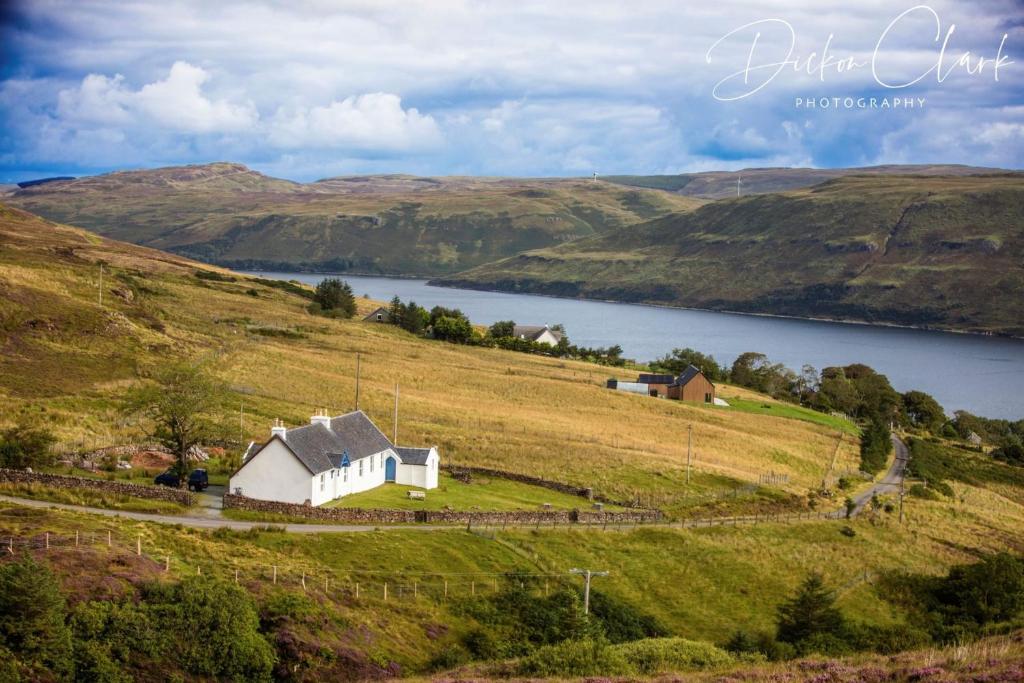 a white house on a hill next to a lake at The Old School House in Carbost