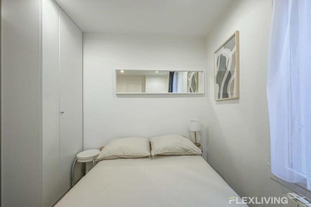 Cette petite chambre blanche comprend un lit et un miroir. dans l'établissement Flexliving - Studio - Bauches, à Paris