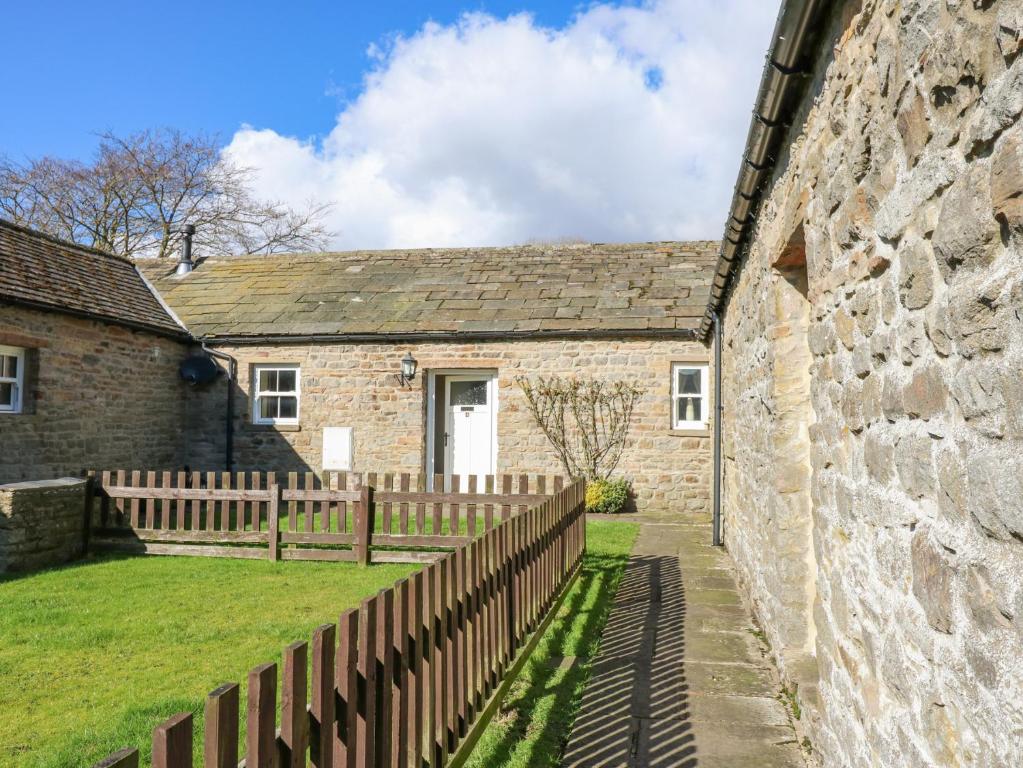 une maison en pierre avec une clôture en bois à côté d'un mur dans l'établissement Pencroft Cottage, à Leyburn