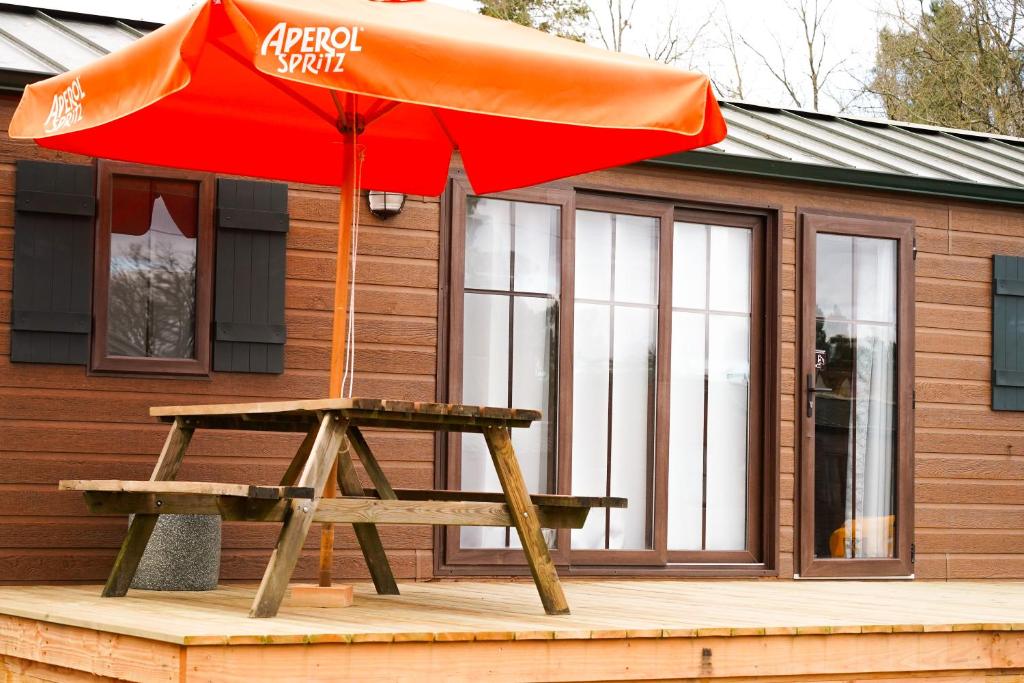 - une table de pique-nique avec un parasol orange sur une terrasse dans l'établissement Pôle Européen du Cheval - Les Cottages de la Futaie, à Yvré-lʼÉvêque