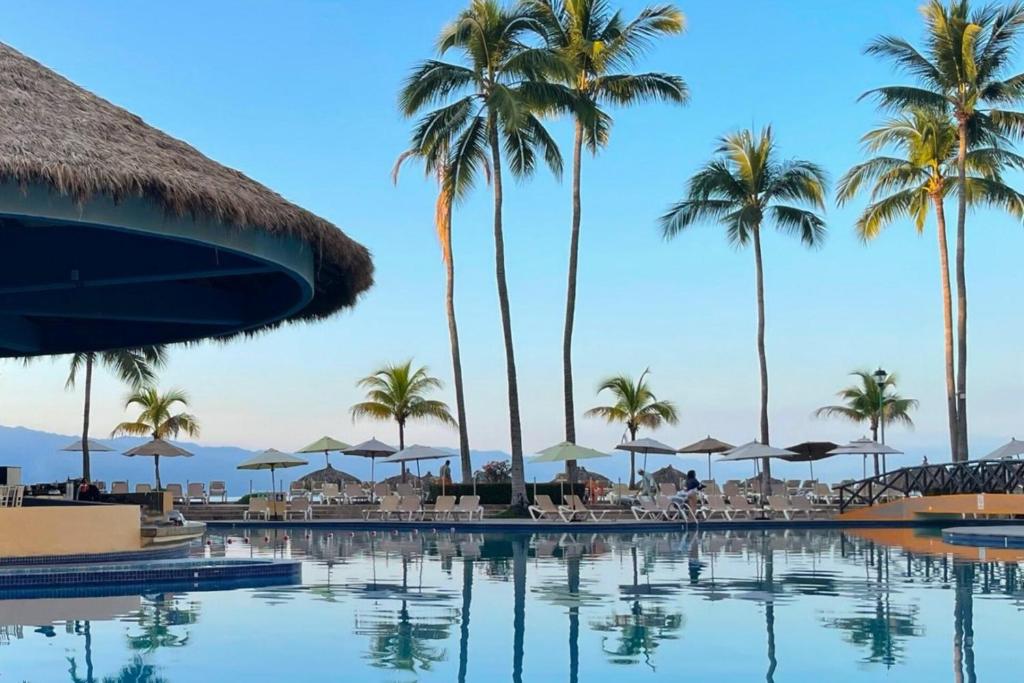 a pool at a resort with palm trees and chairs at Ocean view & direct beach access! in Puerto Vallarta
