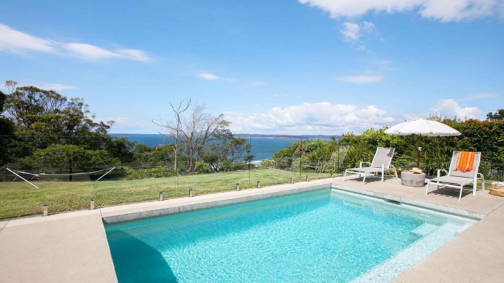 a swimming pool with two chairs and an umbrella at Stunning Ocean Views and Pool in Hardys Bay