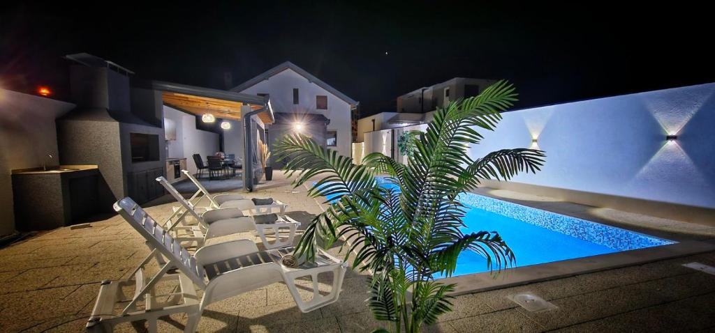 a group of chairs and a swimming pool at night at Villa White Pearl Buna in Hodbina