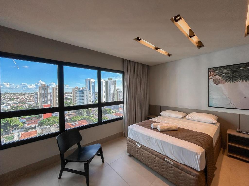 a bedroom with a bed and a chair and large windows at Estúdio Completo e de Luxo ao lado Shopping CG. in Campo Grande