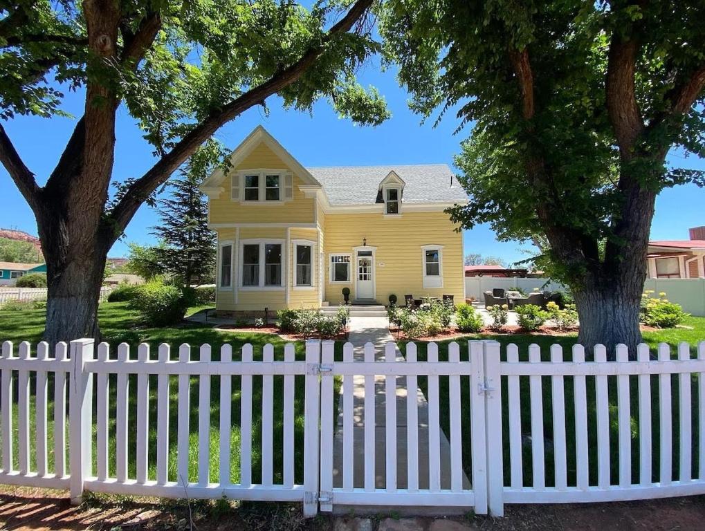 a white picket fence in front of a yellow house at Stunning Historic Home Lots of Space In Town in Kanab