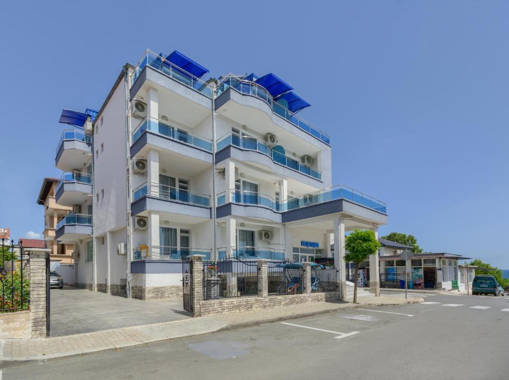 a white building with blue balconies and a parking lot at Siyanie Kiten in Kiten