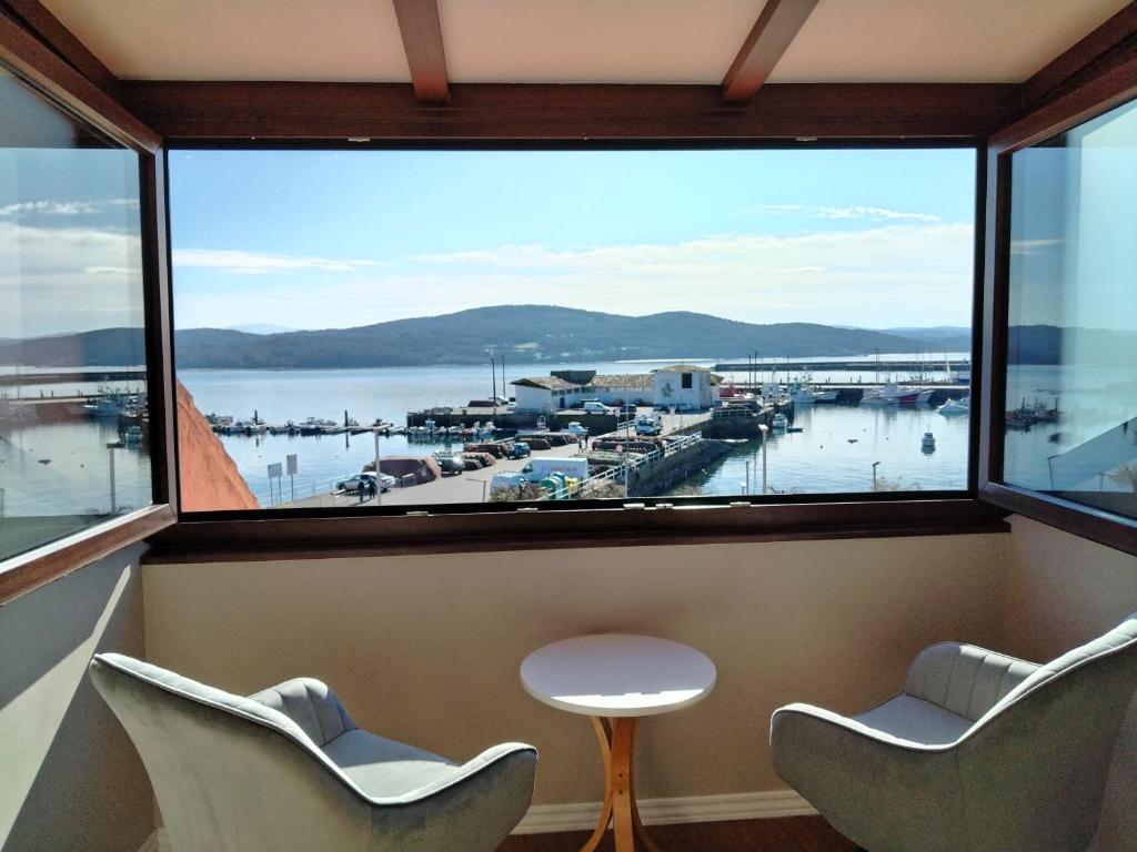 a room with a large window with two chairs and a table at Hotel Puerto Arnela in Camariñas