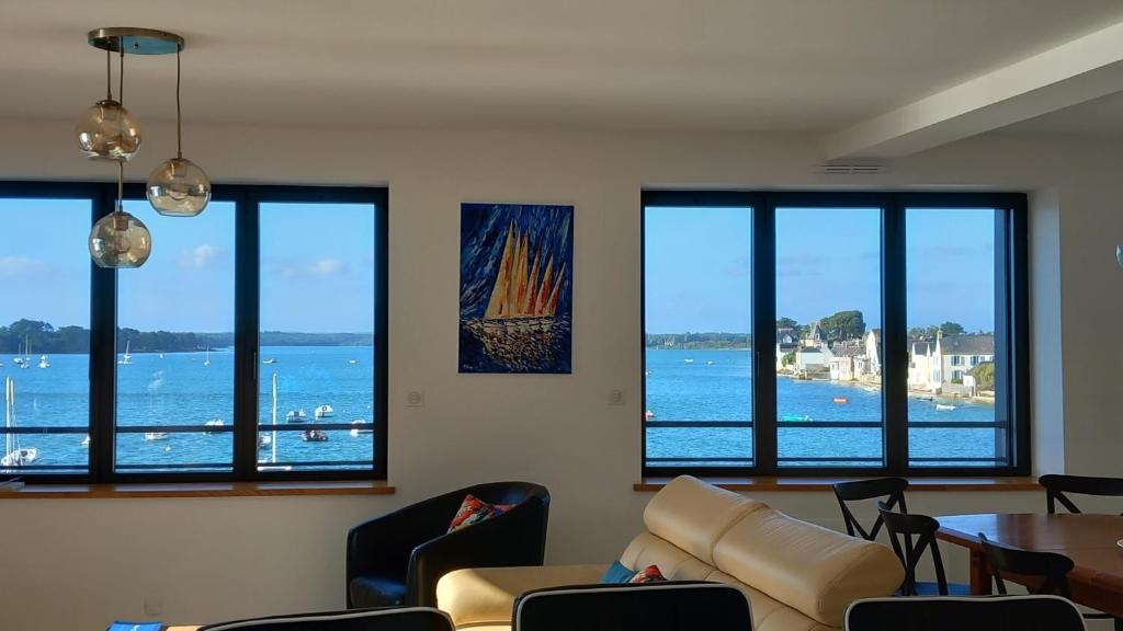 a living room with a couch and a table and windows at Appartement vue sur la mer à l'Ile Tudy ! in Île-Tudy
