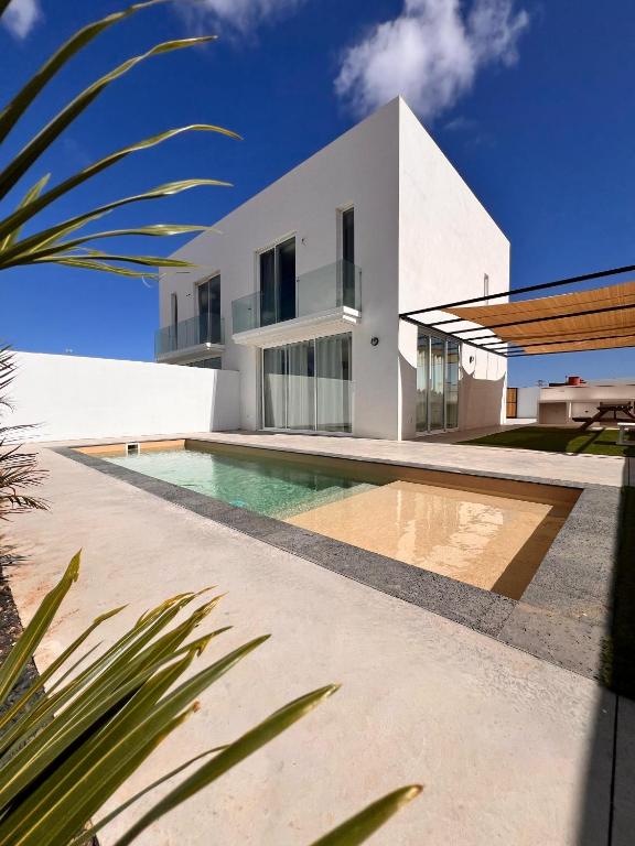 a white house with a swimming pool in front of it at CORRALEJO SURF HOUSE & SCHOOL only SURF in Corralejo