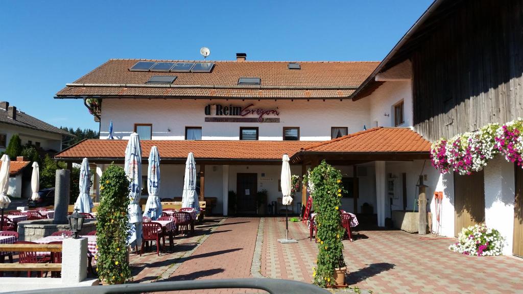 ein Hotel mit Tischen, Stühlen und Sonnenschirmen davor in der Unterkunft Gasthof Pension Gregori in Bad Koetzting