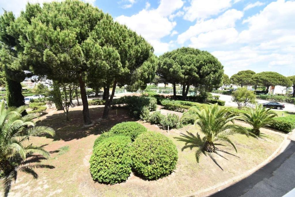 un jardin avec des buissons et des arbres verdoyants et une route dans l'établissement Résidence Le Chabian - Studio cabine 5 couchages dans résidence avec piscine MAE-7121, au Grau-du-Roi