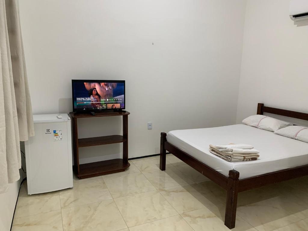 a bedroom with a bed and a tv and a refrigerator at Chalés de Morro Branco in Beberibe