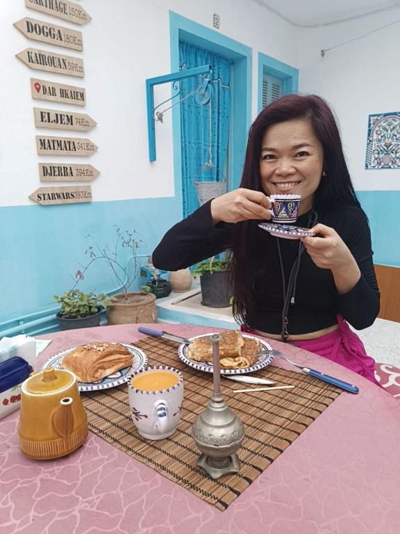 a woman sitting at a table drinking from a cup at Dar Hkaïem in Sousse