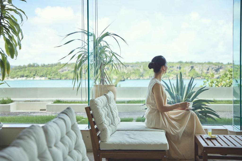 a woman sitting on a couch in front of a window at ANA InterContinental Manza Beach Resort by IHG in Onna