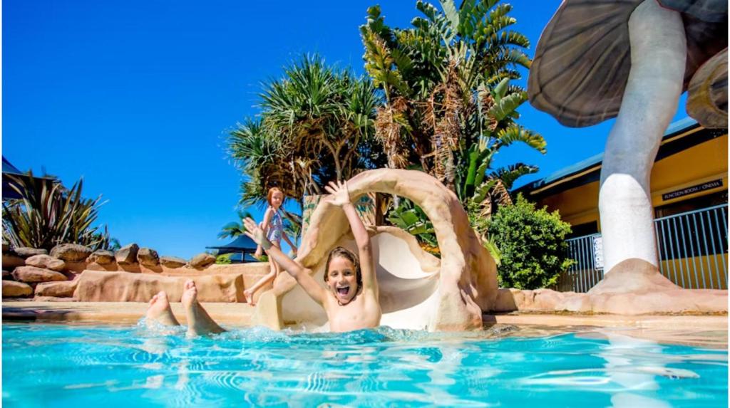 a young child sliding down a water slide in a swimming pool at Discovery Parks - Ballina in Ballina
