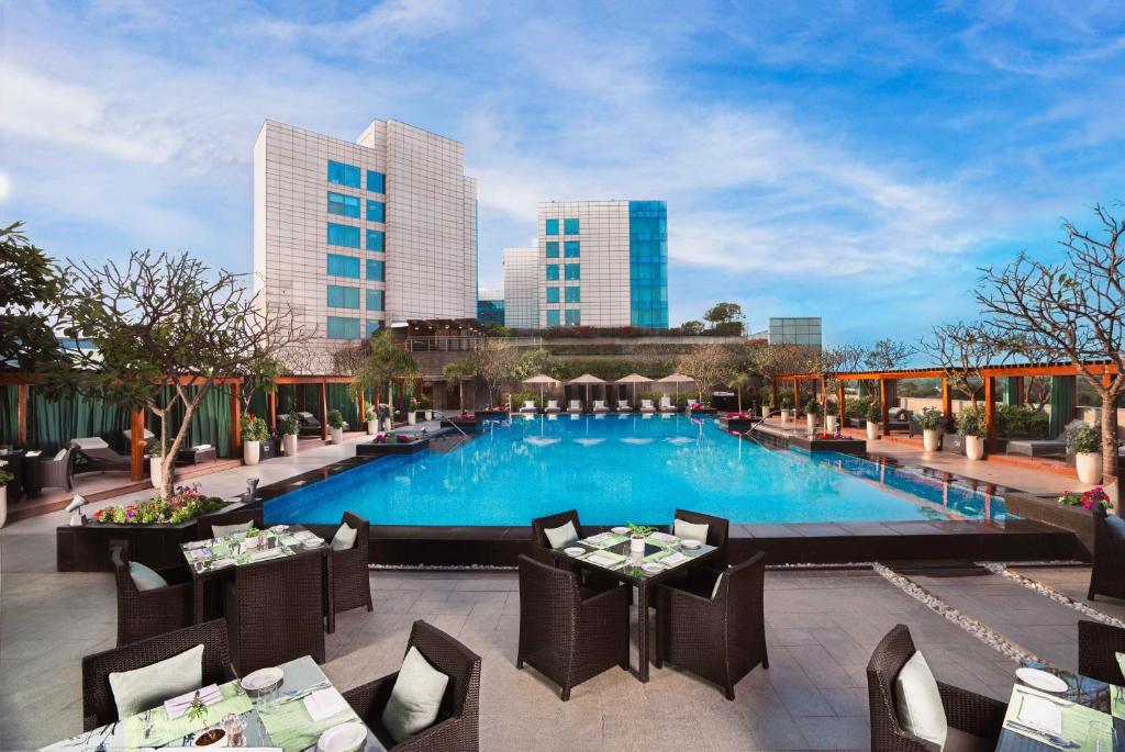 a hotel patio with a pool and tables and chairs at The Leela Ambience Gurugram Hotel & Residences - The Luxury Urban Sanctuary in Gurgaon
