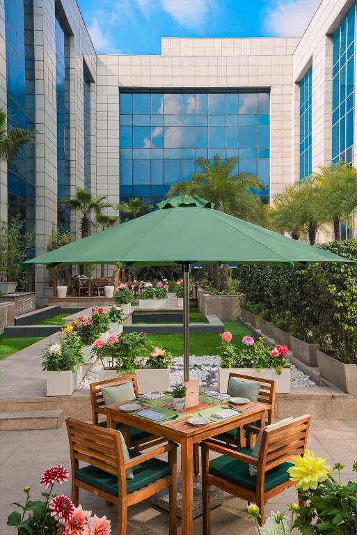 a table with a green umbrella in front of a building at The Leela Ambience Gurugram Hotel & Residences - The Luxury Urban Sanctuary in Gurgaon