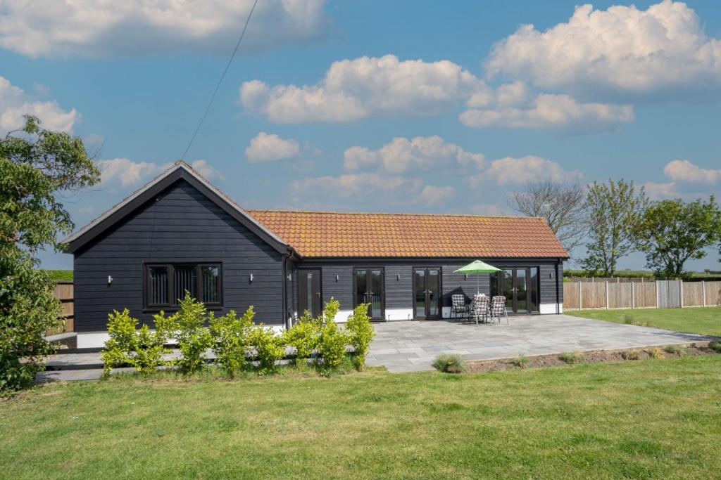 a black house with a patio in a yard at The Old Stable by Winterton Cottages in Hemsby