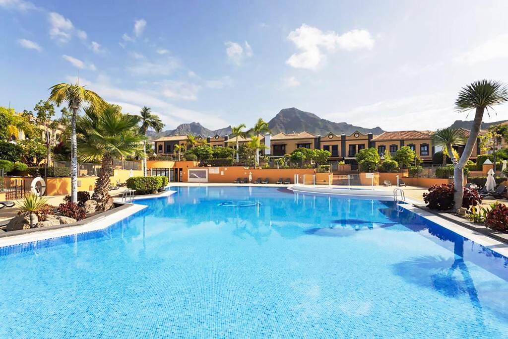 ein großer blauer Pool mit Palmen und Gebäuden in der Unterkunft Exclusive Townhouse in Central Plaza del Duque Close to the Beach in Adeje