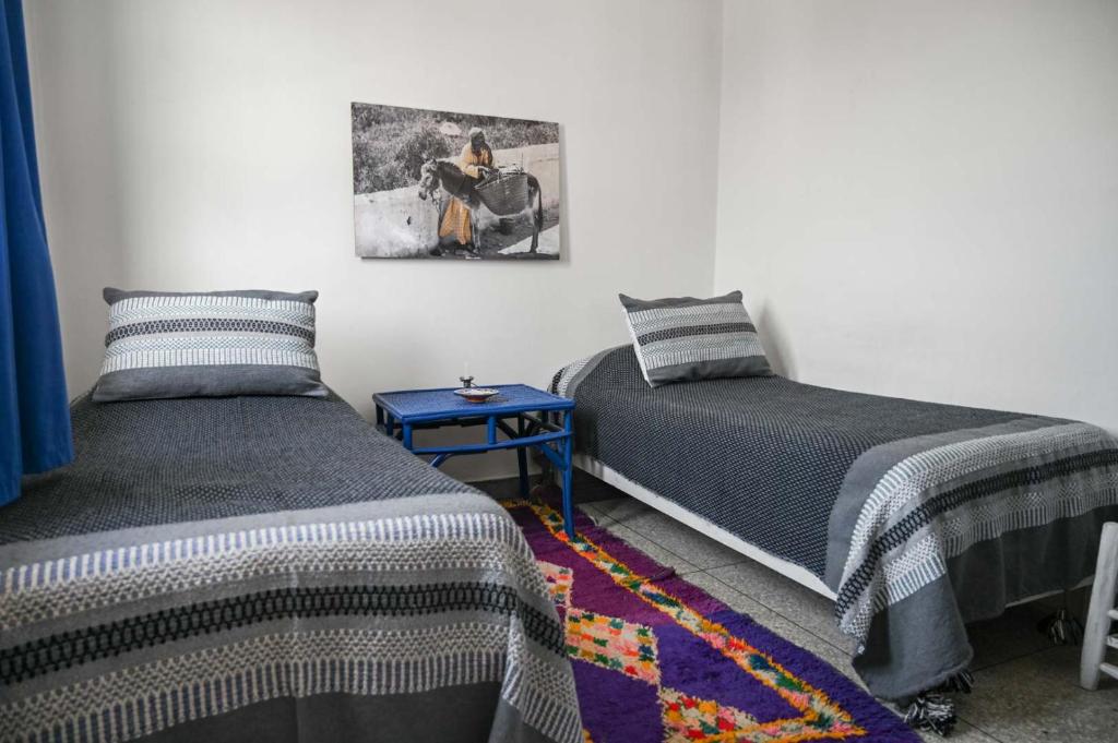 a bedroom with two beds and a painting on the wall at Hotel-Restaurant Le Kaouki in Sidi Kaouki