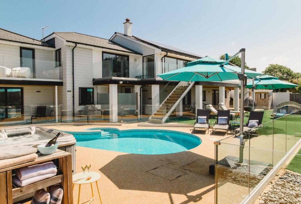 a swimming pool with an umbrella and chairs and a house at Heron House in Newquay