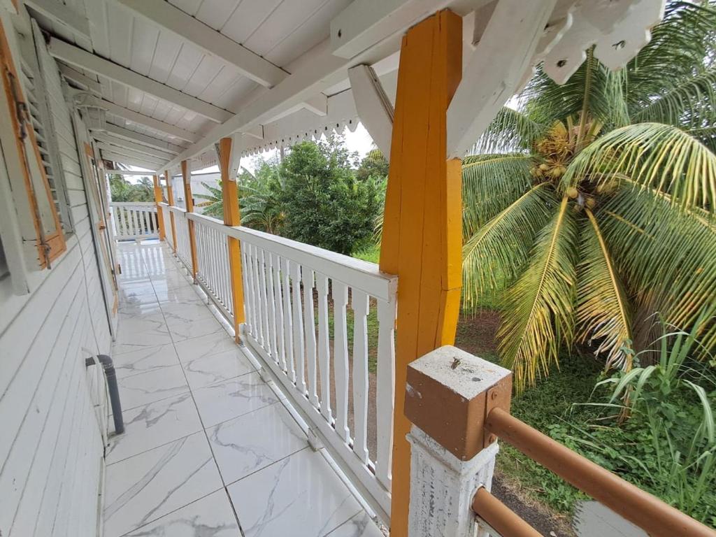 a porch with a white fence and a palm tree at Le Bon Logis du Carbet in Capesterre-Belle-Eau