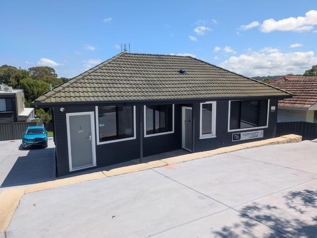 une petite maison noire avec une voiture garée dans une allée dans l'établissement Northcott Lodge, à Adamstown