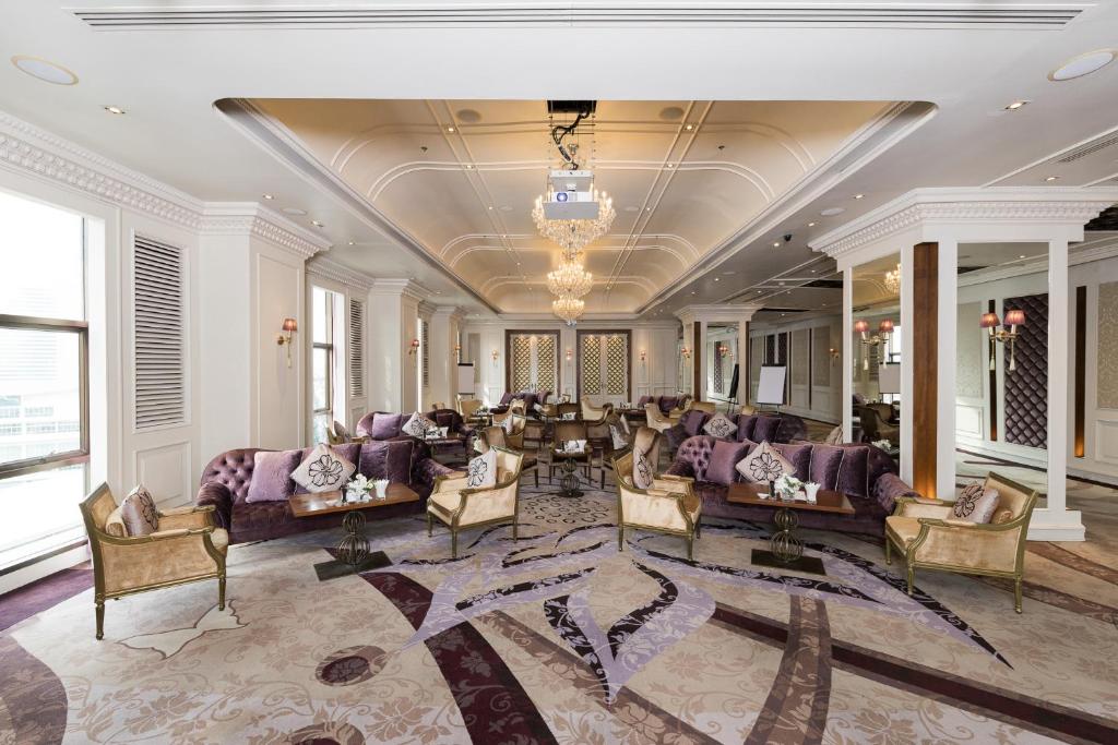 A grand lounge offers clusters of purple sofas and armchairs beneath chandeliers in a bright classical interior.