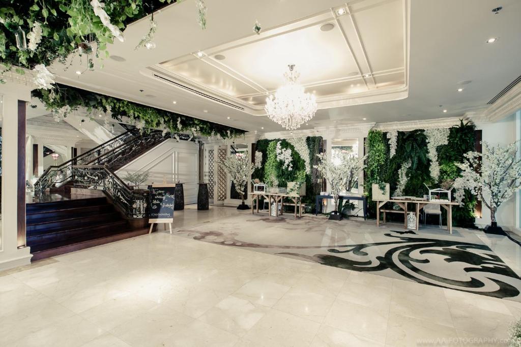 A grand marble event foyer with a sweeping staircase and leafy floral decoration.