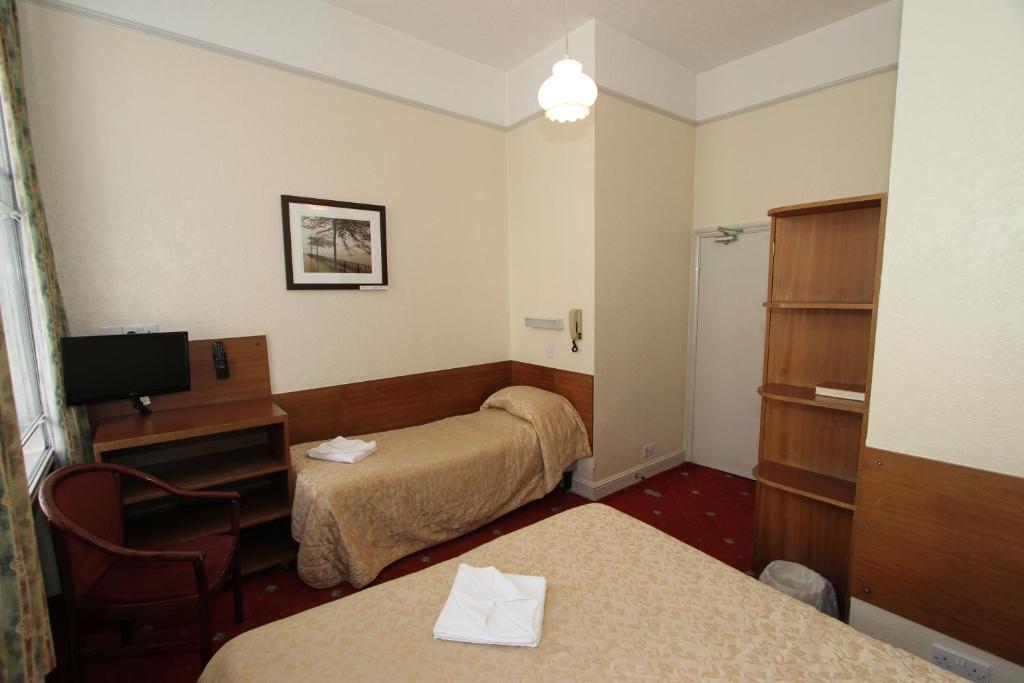 a room with two beds and a desk and a television at Ridgemount Hotel in London