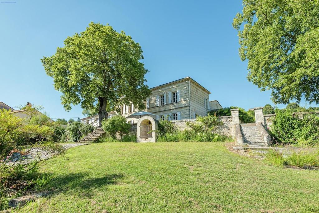une vieille maison avec un arbre dans une cour dans l'établissement Demeure en pierre au cœur des vignobles de Bordeaux, à Saint-Germain-de-la-Rivière