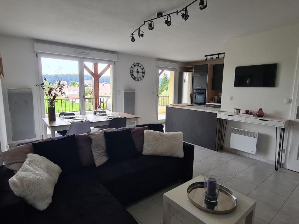 a living room with a black couch and a kitchen at O'fil du Doubs Apartment in Labergement-Sainte-Marie