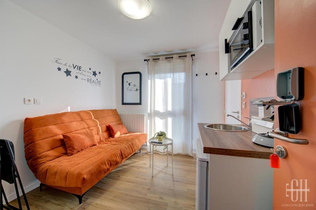 un canapé orange dans un salon avec une cuisine dans l'établissement Mars - Proche A10 - 2V - Parking, à Saint-Pierre-des-Corps